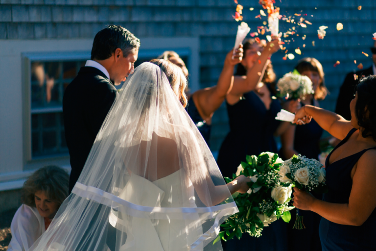 a recently married man and woman walking towards a group of people tossing flower petals