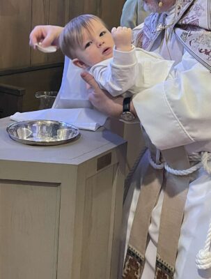 a baby dressed in white being lowered for baptism