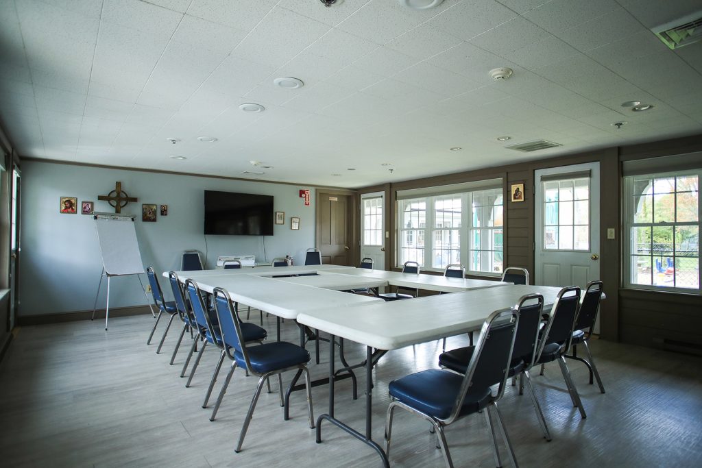 a room with white tables, blue chairs and a tv screen mounted on the wall