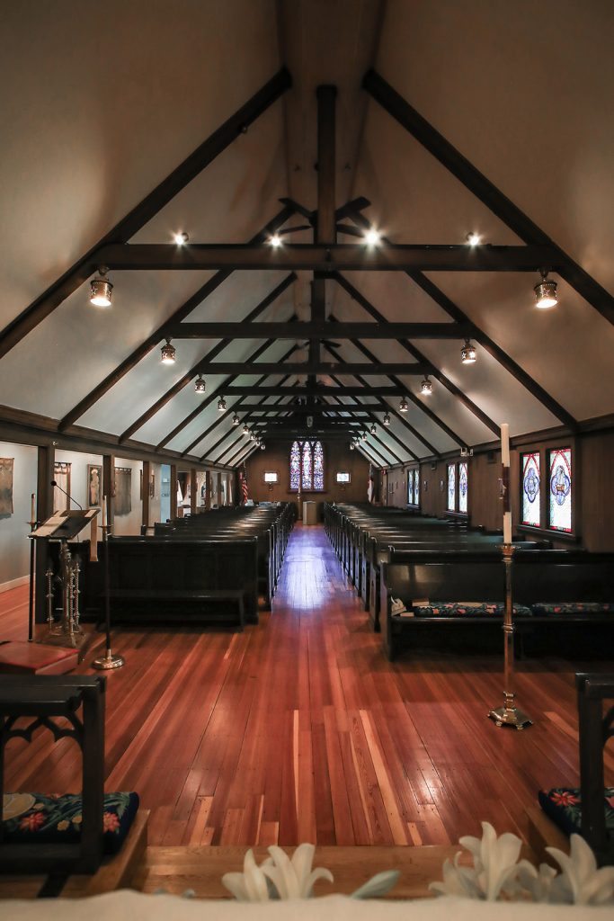 The inside of a church with dark shiny wood floors, stained glass windws, and dark wooden pews