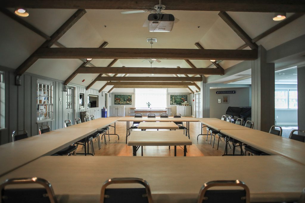 A large room with wooden beams and large table set up in a rectangle with chair